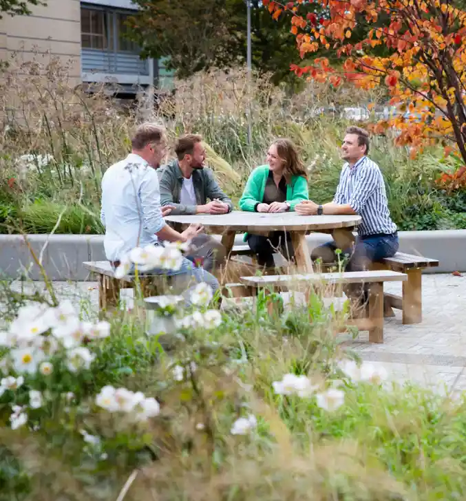 Collega's Stevin lachen aan picknicktafel in de buitenlucht met bloemen om zich heen